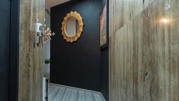 Un couloir étroit doté d’un plancher en bois, d’un mur noir et d’un miroir décoratif en forme de soleil rayonnant.