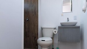 Une petite salle de bain avec des toilettes blanches, un lavabo surmonté d’un miroir et une porte en bois.