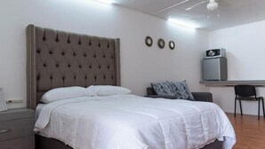 Une chambre à coucher avec un grand lit, une table de chevet, un bureau avec une chaise et un ventilateur de plafond.