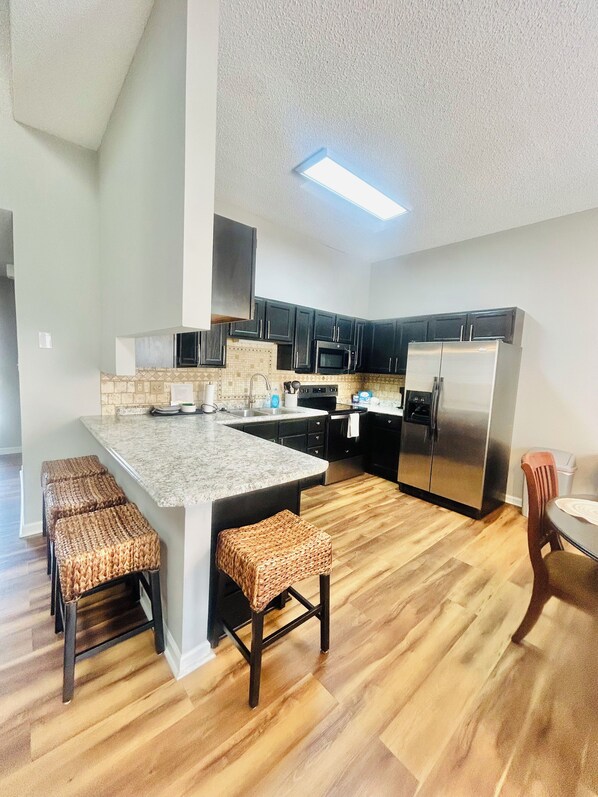 A modern kitchen with a central island, dark cabinetry, stainless steel appliances, and a wooden floor.