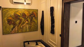A hallway with a large abstract painting, a wall-mounted sculpture, and a door with a dark frame. - The Westbury Inn Hotels and Apartments (Abuja)