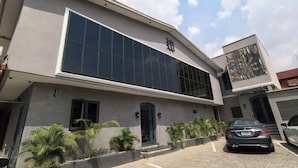 A modern building with a large glass facade, a prominent entrance with a decorative door, and a parking area with a few cars. - The Westbury Inn Hotels and Apartments (Abuja)