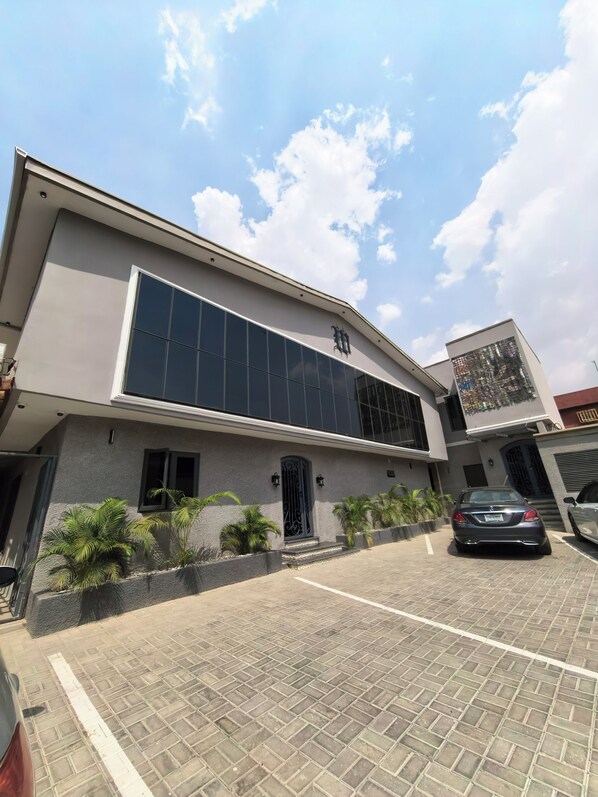 A modern building with a large glass facade, a prominent entrance with a decorative door, and a parking area with a few cars. - The Westbury Inn Hotels and Apartments (Abuja)