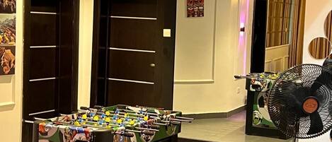 A room with a foosball table, a fan, and a door with a mirror.