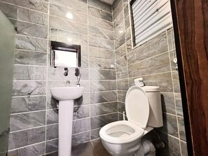 Un baño con pared de azulejos de mármol, un lavamanos pedestal y un inodoro.