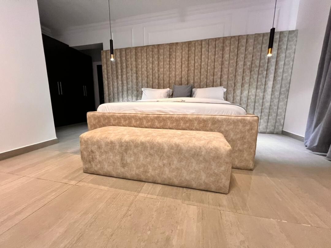 A modern bedroom with a large bed, a bench, and a patterned headboard.