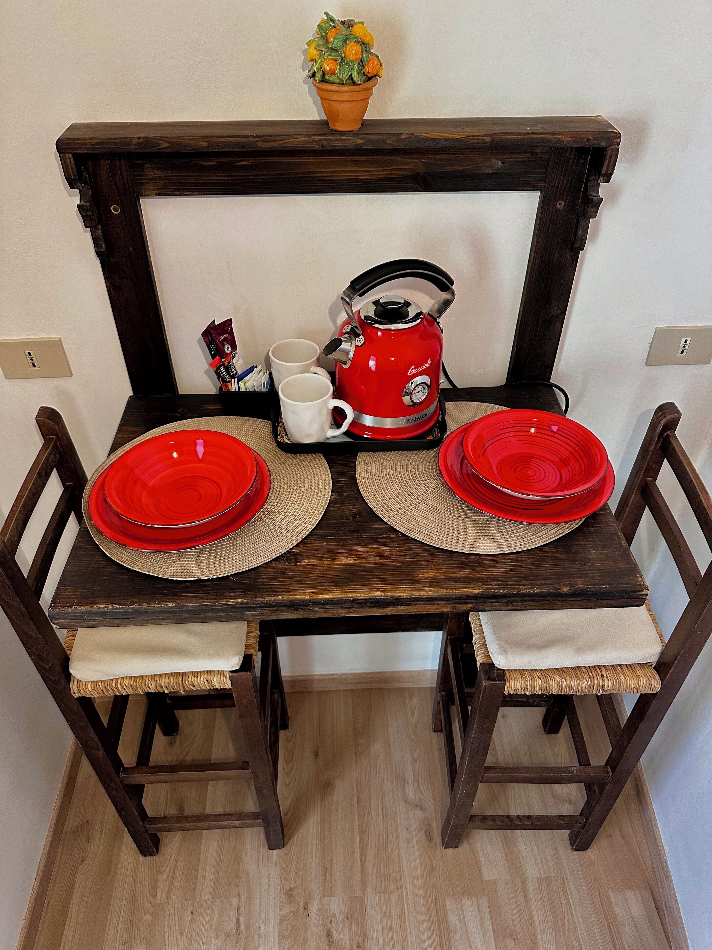 A wooden dining table with two red plates, two white mugs, and a red kettle.