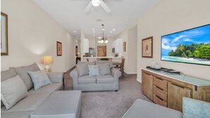 A modern living room with a grey sofa, ottoman, and a flat-screen TV mounted on the wall.