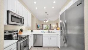 A modern kitchen with white cabinets, stainless steel appliances, and a tiled floor.