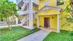 A yellow multi-story building with a white exterior, a front door, and a staircase leading to the upper floors.