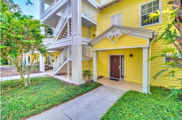 A yellow multi-story building with a white exterior, a front door, and a staircase leading to the upper floors.