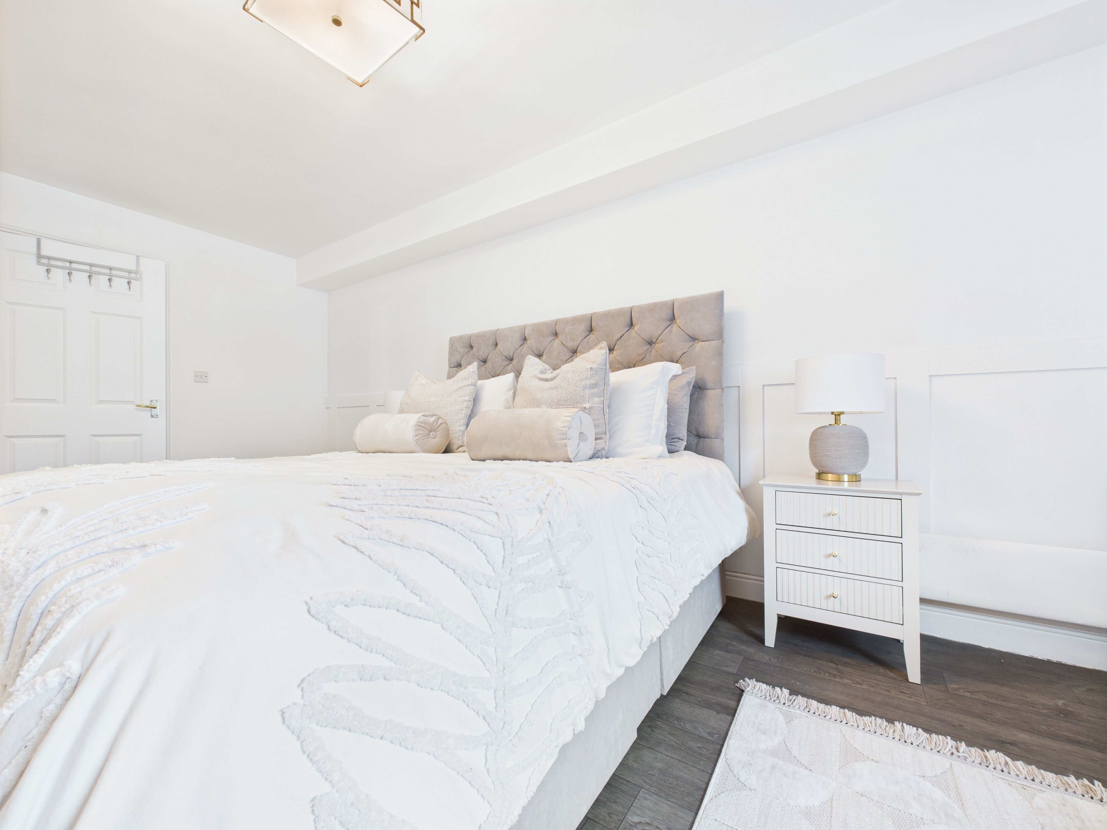A bedroom with a large bed, a nightstand with a lamp, and a door.
