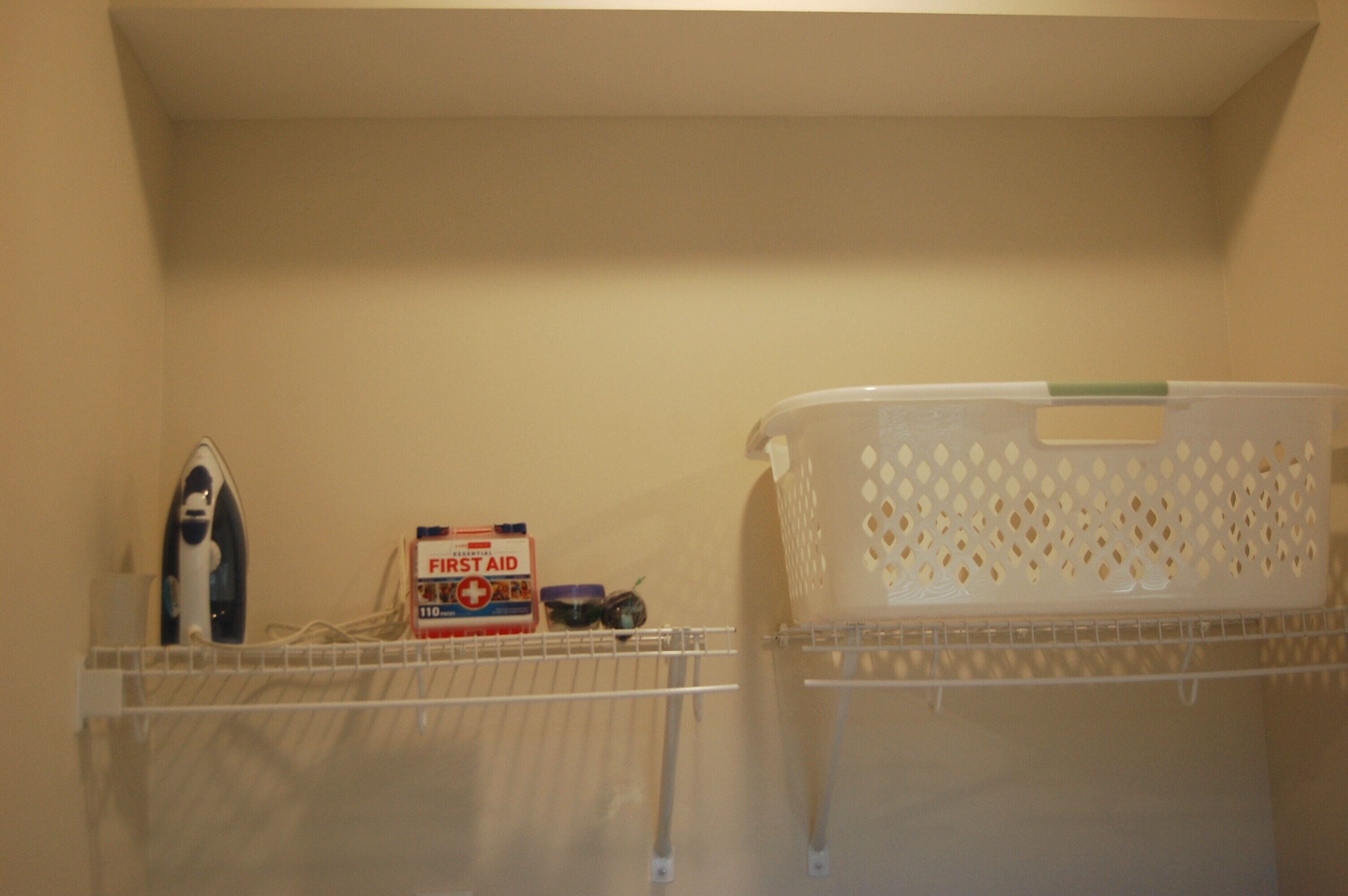 Un espace dédié à la lessive, avec un panier à linge, un fer à repasser et une trousse de premiers secours sur une étagère.