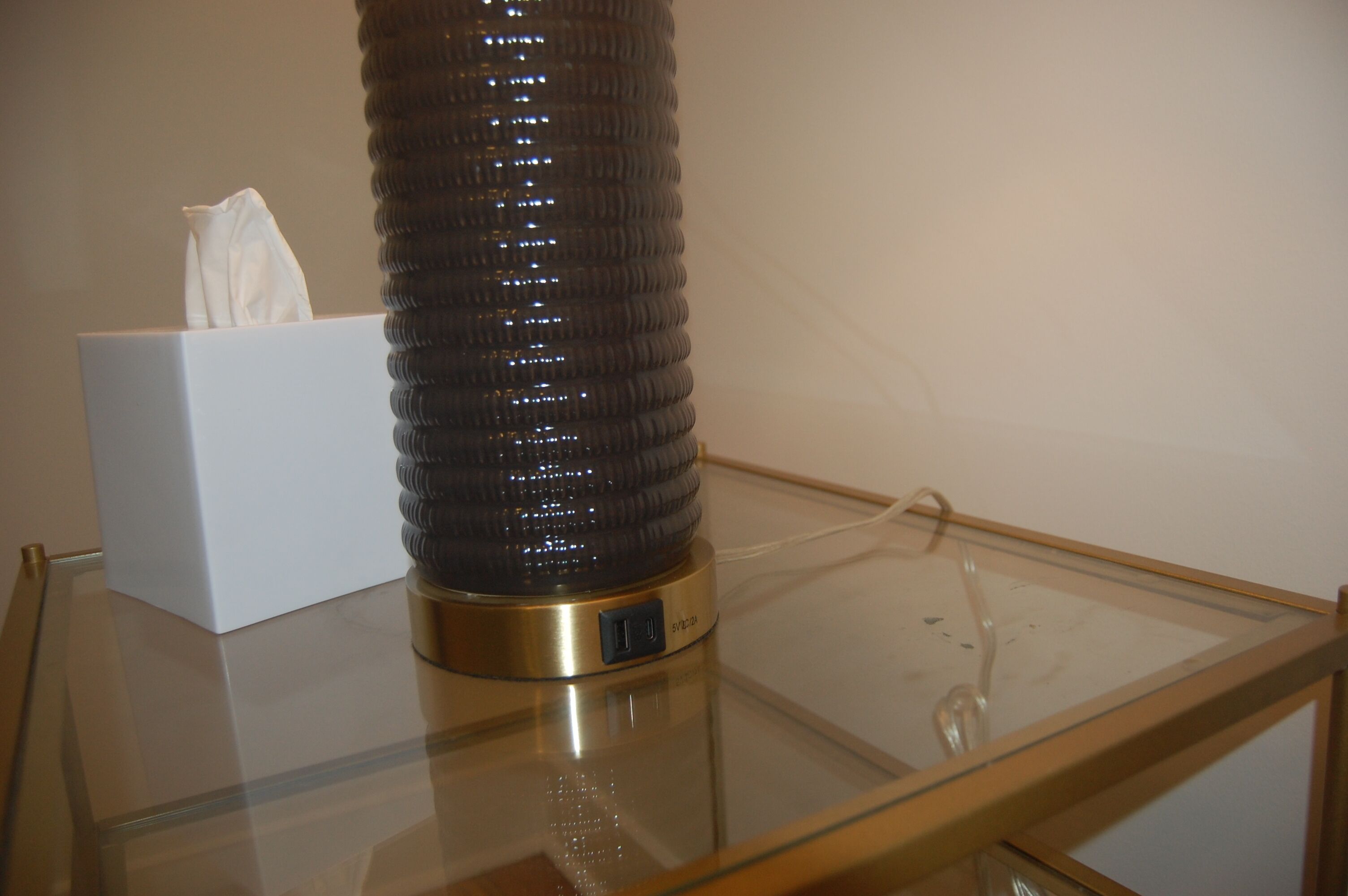 Une table en verre sur laquelle se trouvent un boîte à mouchoirs et un objet cylindrique.