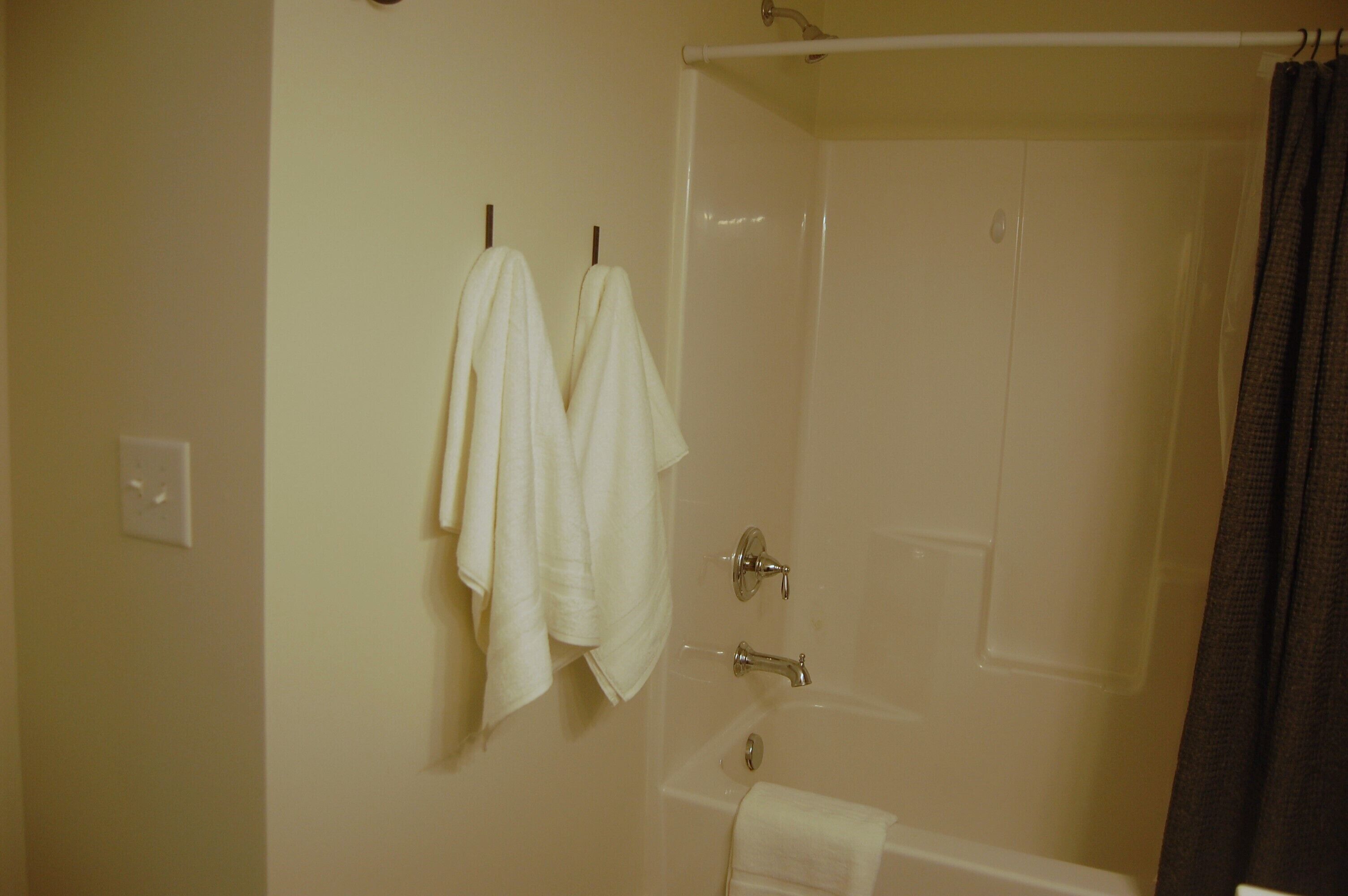 Un baño con bañera, cortina de ducha y dos toallas colgadas en ganchos.