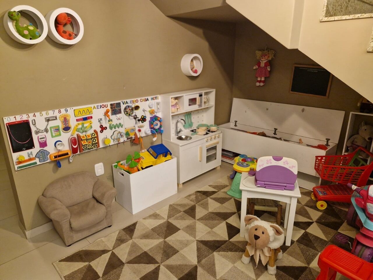 Um espaço de brincar com uma cozinha de brinquedo, brinquedos e um tapete estampado.