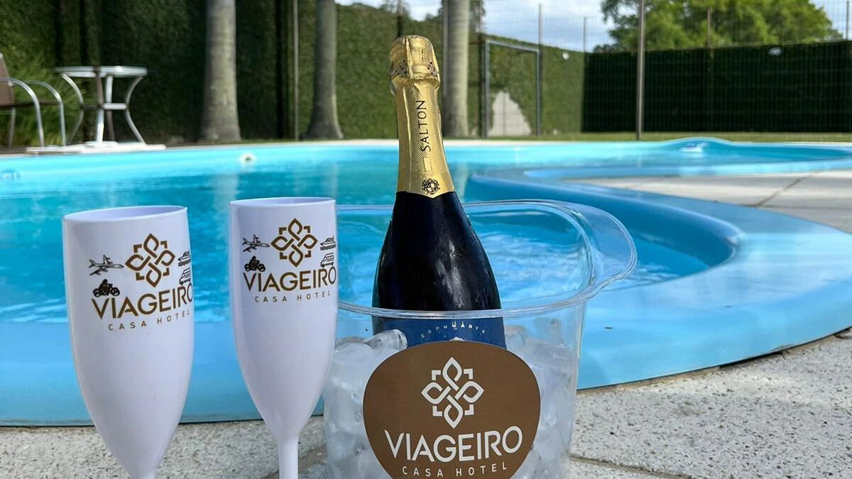 Dos copas de champán y una botella en un cubo de hielo transparente con el logotipo 'Viageiro Casa Hotel', junto a una piscina.