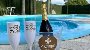 Twee champagneglazen en een champagnefles in een ijsbak van glas, met het logo 'Viageiro Casa Hotel', geplaatst bij een zwembad.