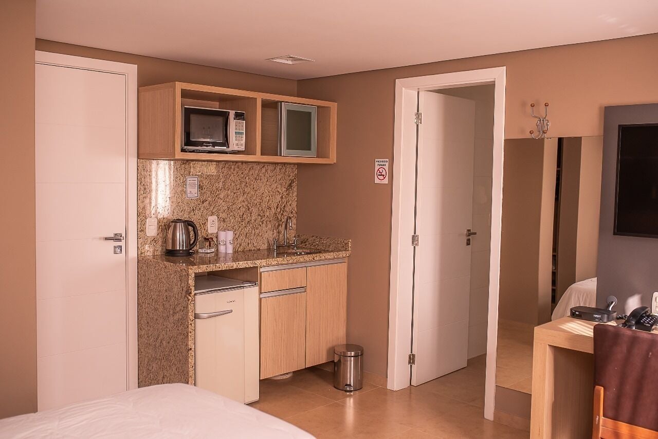 Una habitación de hotel compacta con kitchenette, cama, escritorio y baño.