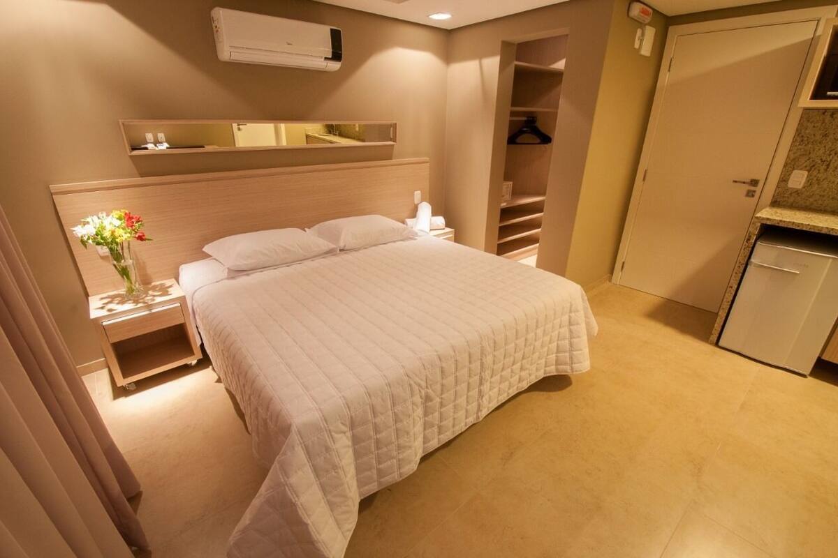 A hotel room with a bed, bedside table, nightstand, dresser, and a walk-in closet.