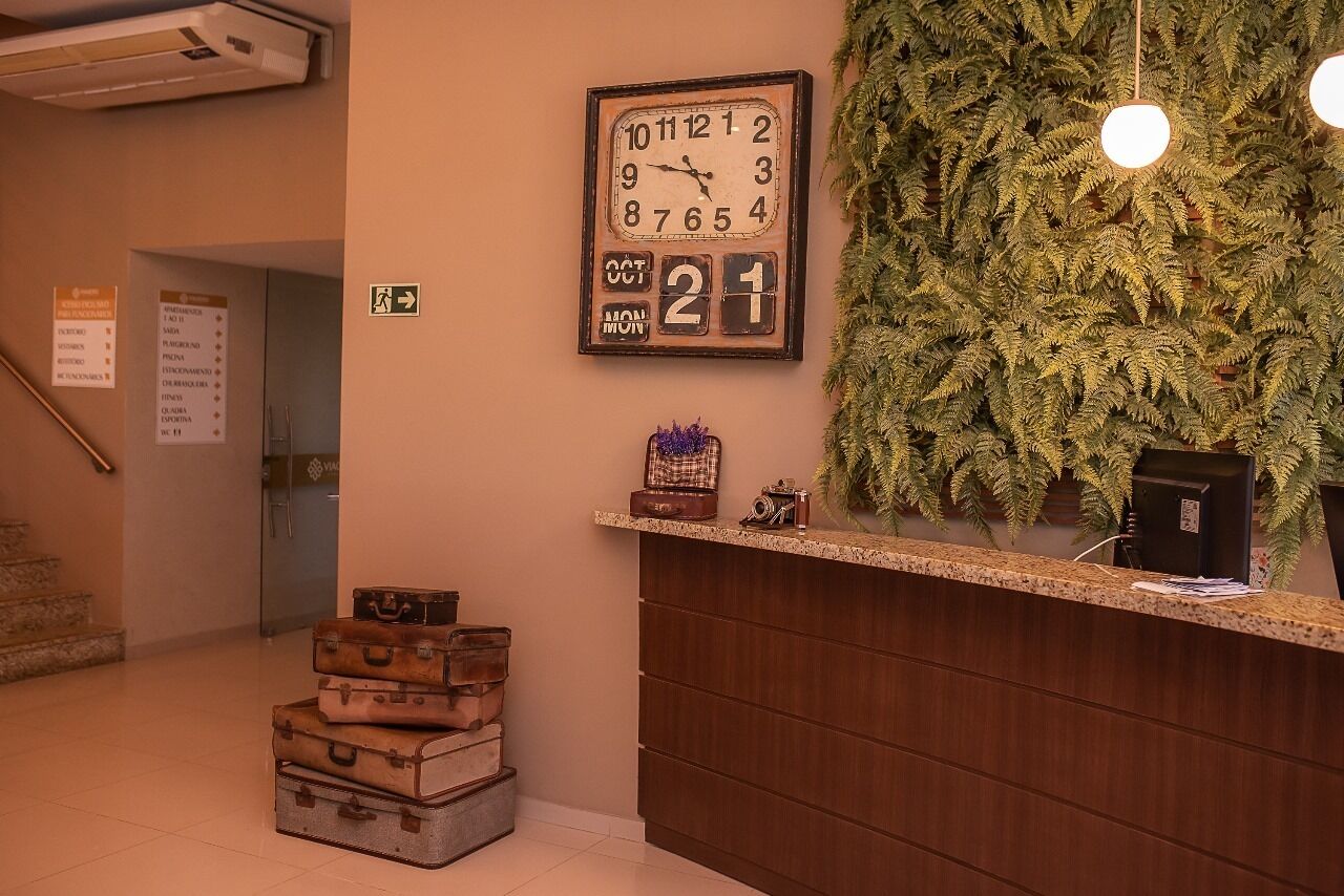 A reception area with a wooden desk, a clock, and a fern wall.