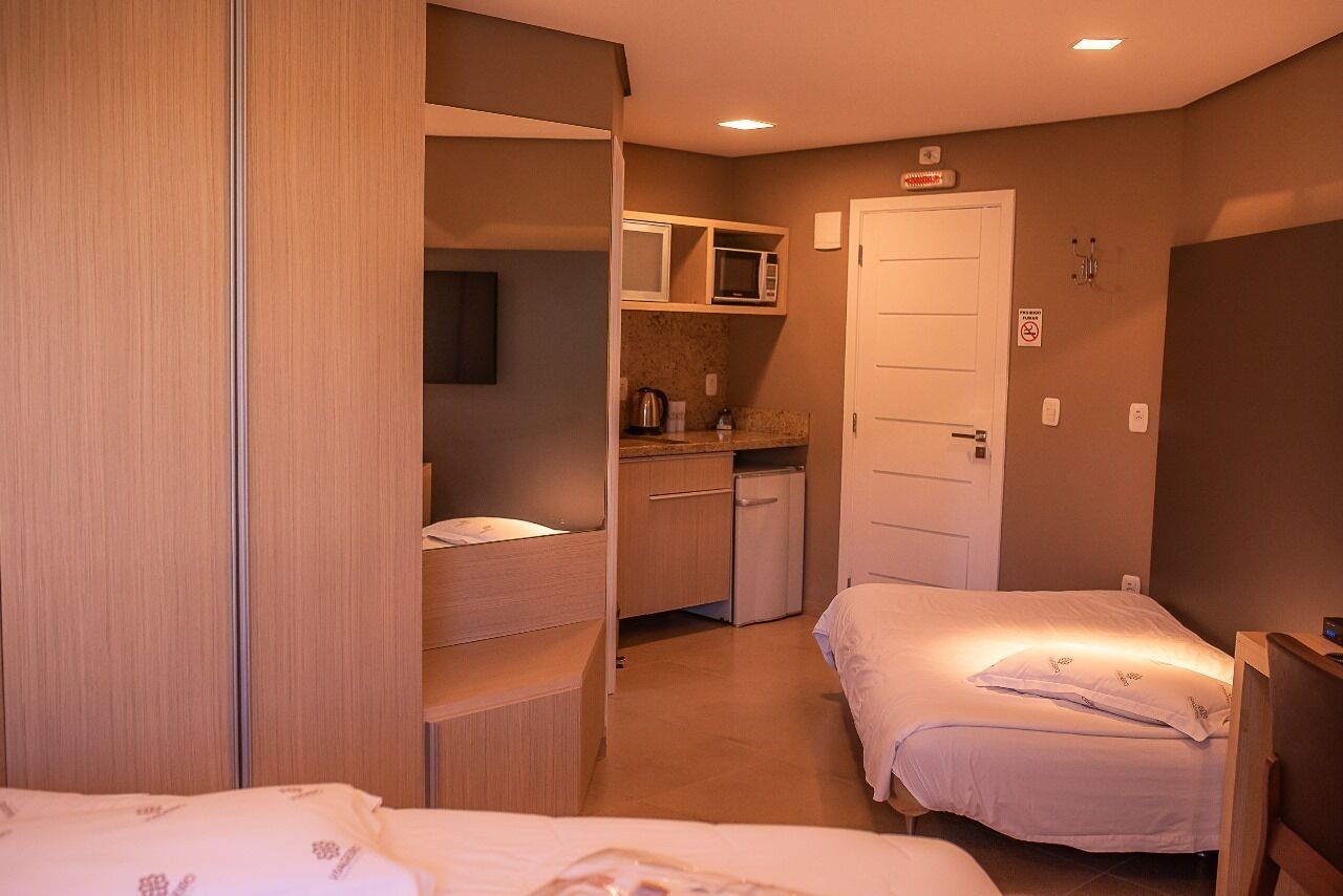 Une chambre d’hôtel compacte comprenant deux lits simples, une kitchenette, une armoire et une porte avec une pancarte.