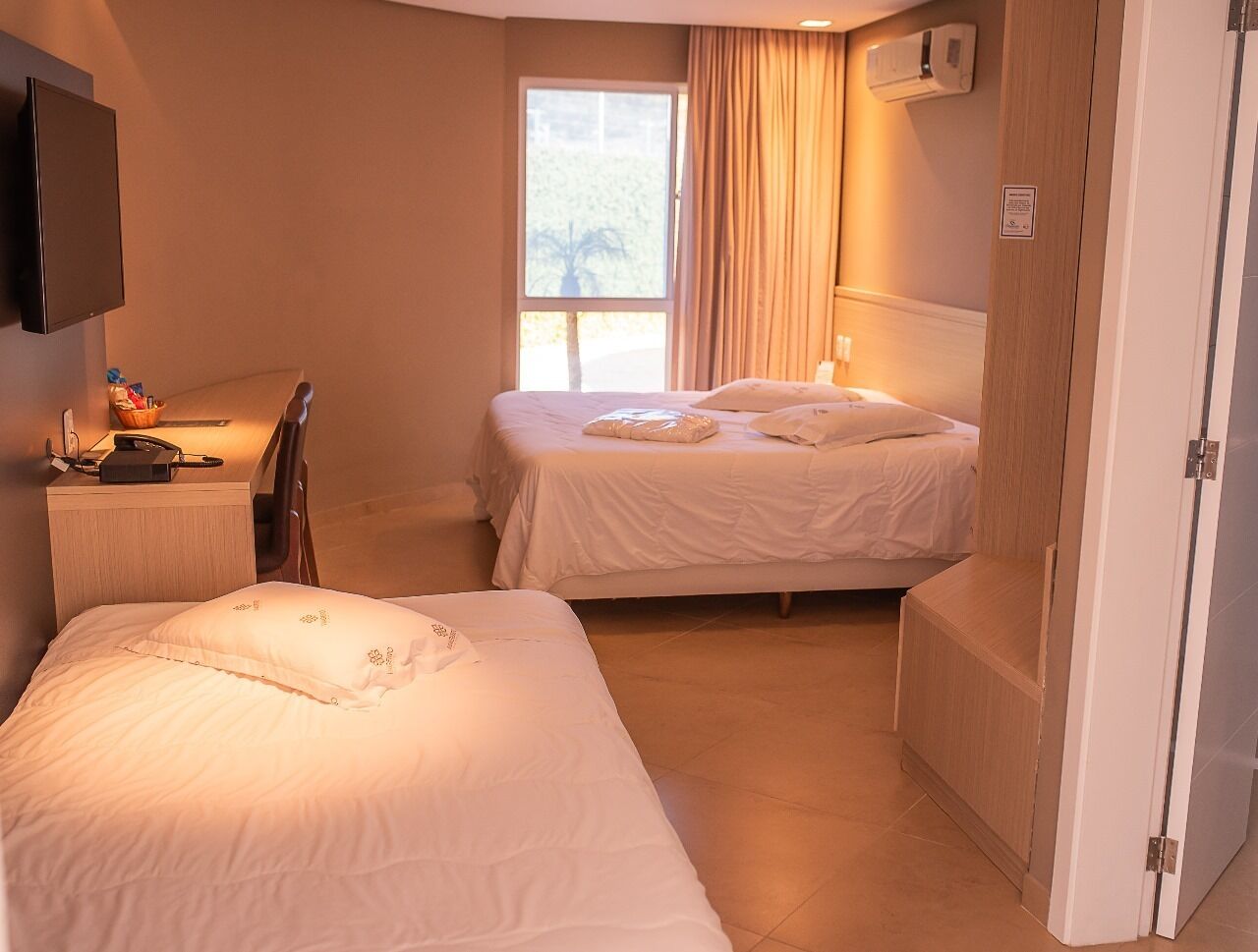 A hotel room with two beds, a desk, a chair, a TV, and a window with curtains.