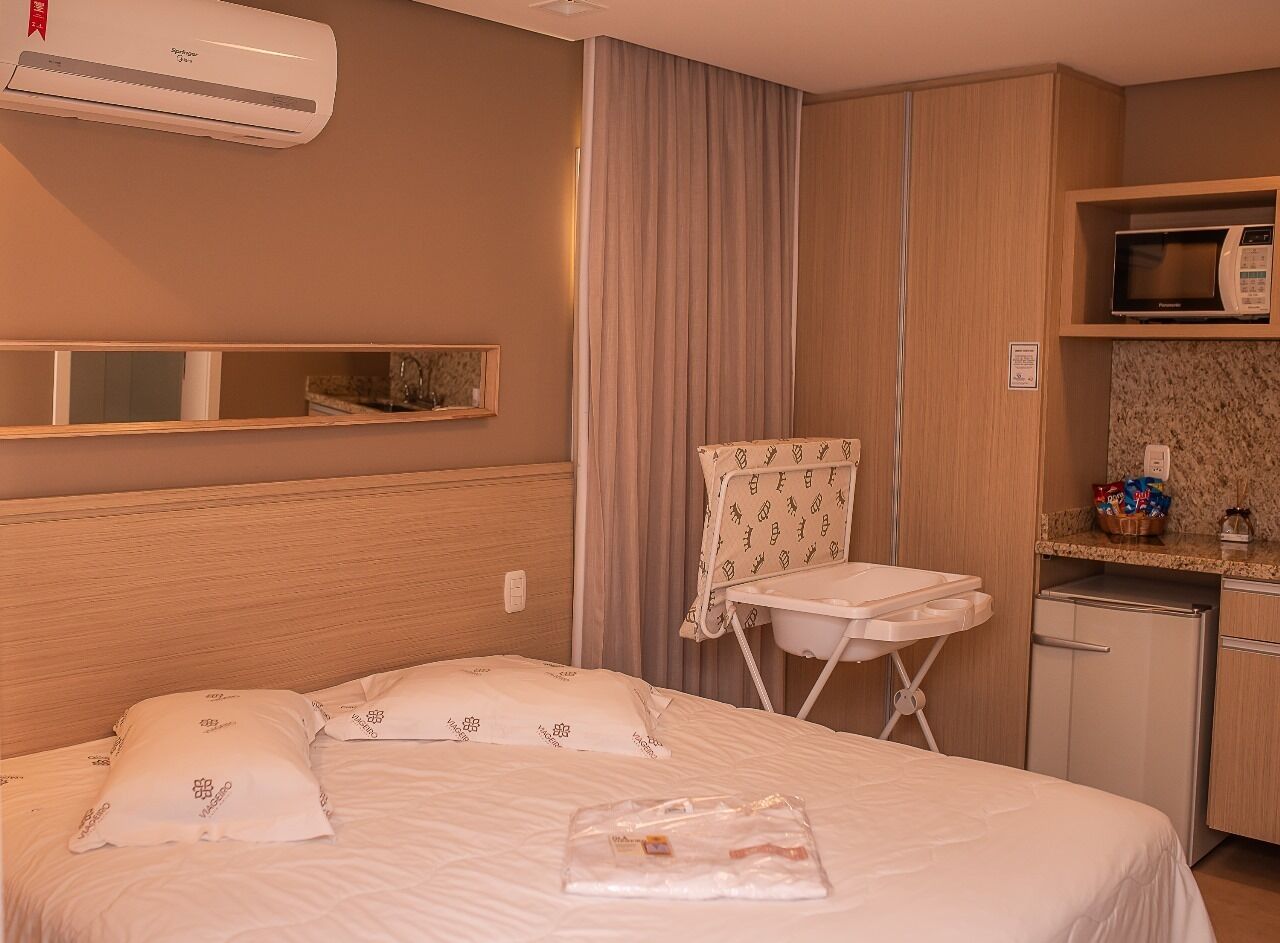 A hotel room with a bed, a small kitchenette, an ironing board, and a microwave.