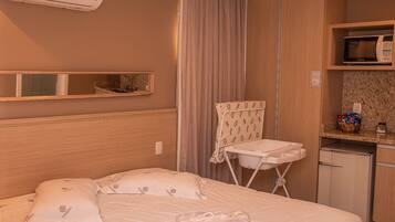 A hotel room with a bed, a small kitchenette, an ironing board, and a microwave.