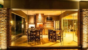A modern kitchen with a brick wall, a TV mounted above the counter, and a dining area with chairs and a table. - Viageiro Hotel (Pelotas)