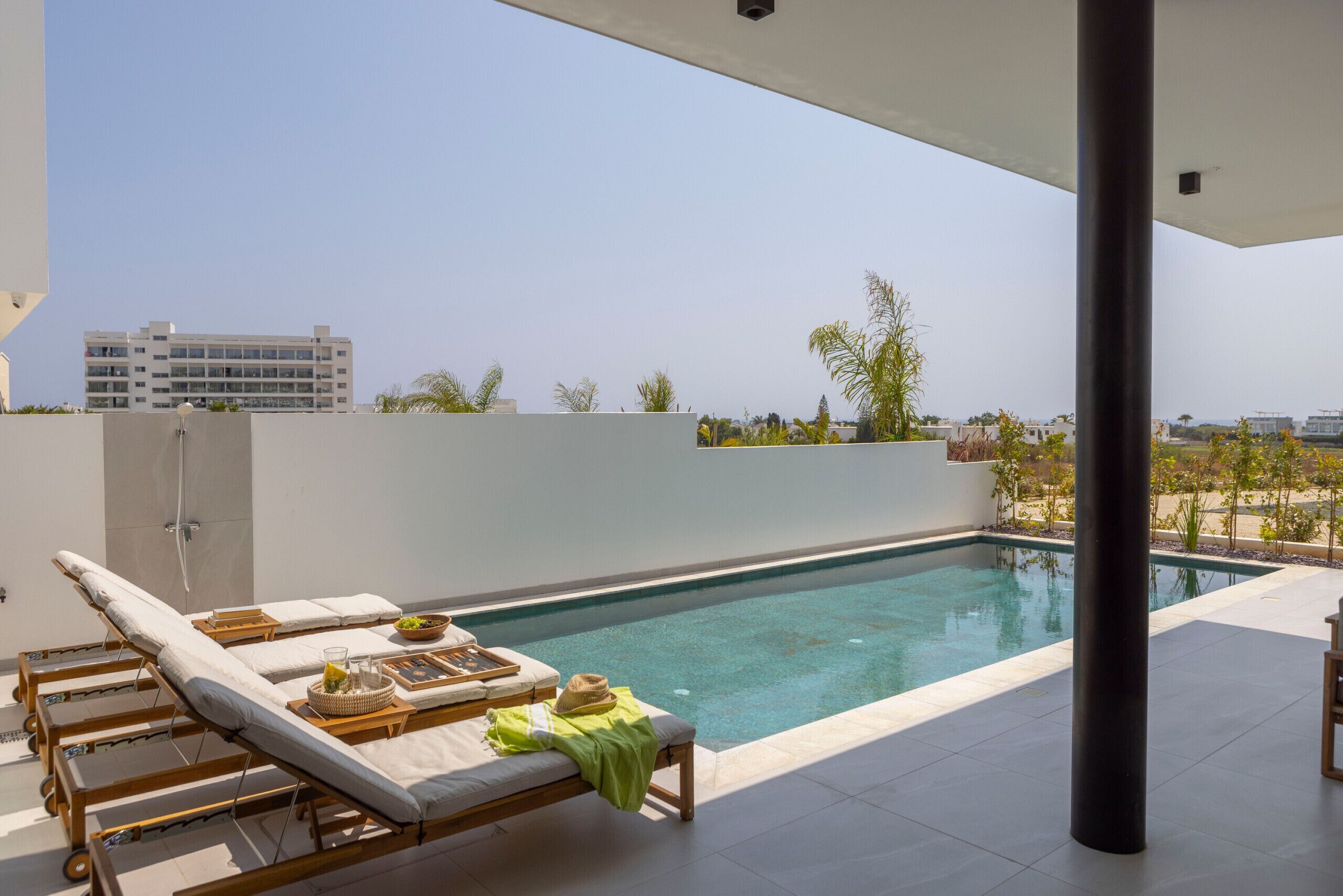 Zona de piscina en la azotea con tumbonas, una mesa pequeña con un cuenco de fruta y vistas a un paisaje urbano.