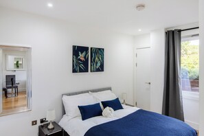 A bedroom with a bed, two wall-mounted paintings, a bedside table with a lamp, and a window with curtains.
