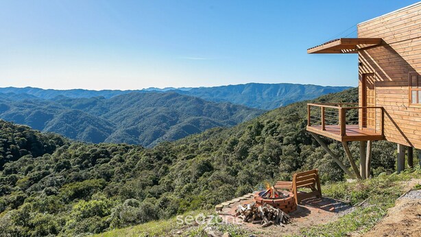 A wooden cabin with a deck overlooking a mountainous landscape.