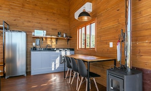 A compact kitchen with a refrigerator, microwave, coffee maker, and stove. There is a dining table with chairs and a window providing a view of the outdoors.