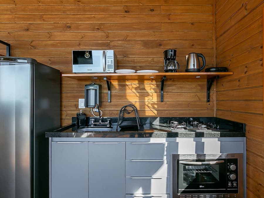 A compact kitchen with a refrigerator, microwave, coffee maker, kettle, and oven.