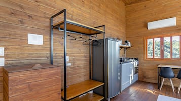 A compact kitchen with wooden walls, a built-in refrigerator, a stove, and a window providing a view of the outdoors.