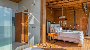 A modern bedroom with a glass shower enclosure, a wooden ceiling, and a bed with a white comforter.