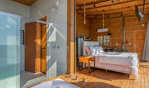 Un dormitorio moderno con cabina de ducha de vidrio, techo de madera y cama con edredón blanco.