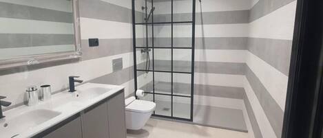 Un baño moderno con diseño de pared a rayas, cabina de ducha de vidrio, inodoro blanco y tocador con espejo y lavabo.