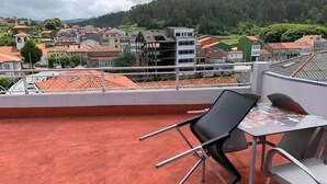 A rooftop terrace with a table and chairs, overlooking a residential area with houses and a hill in the background.