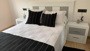A neatly made bed with a striped black and white bedspread, two black and white pillows, and a white headboard. There are two bedside tables with drawers and a lamp on one.