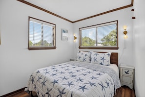 Une chambre à coucher avec un lit, deux fenêtres, une table de chevet et des appliques murales.