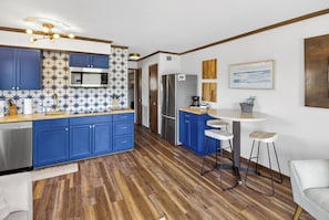 A modern kitchen with blue cabinets, a microwave, a refrigerator, and a small dining area with stools.