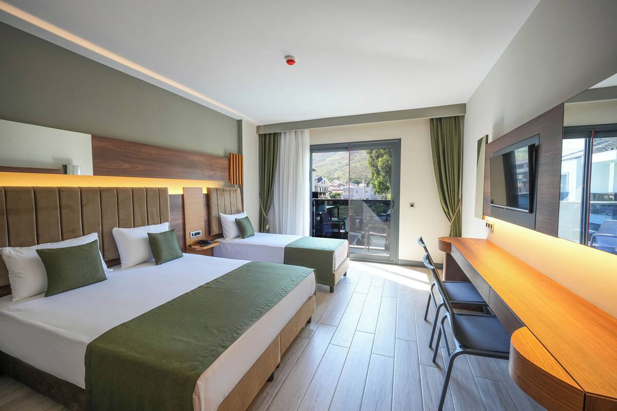Una camera d'albergo con due letti, una scrivania e un televisore.