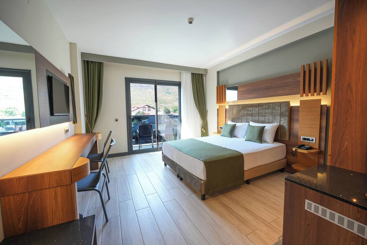 Una camera d'albergo moderna con un letto, una scrivania, una sedia, una televisione e vista sull'esterno.
