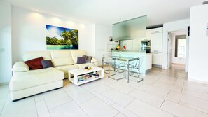 Uma sala de estar moderna com um sofá branco, uma mesa de centro de vidro e um espaço de jantar com mesa e cadeiras de vidro.