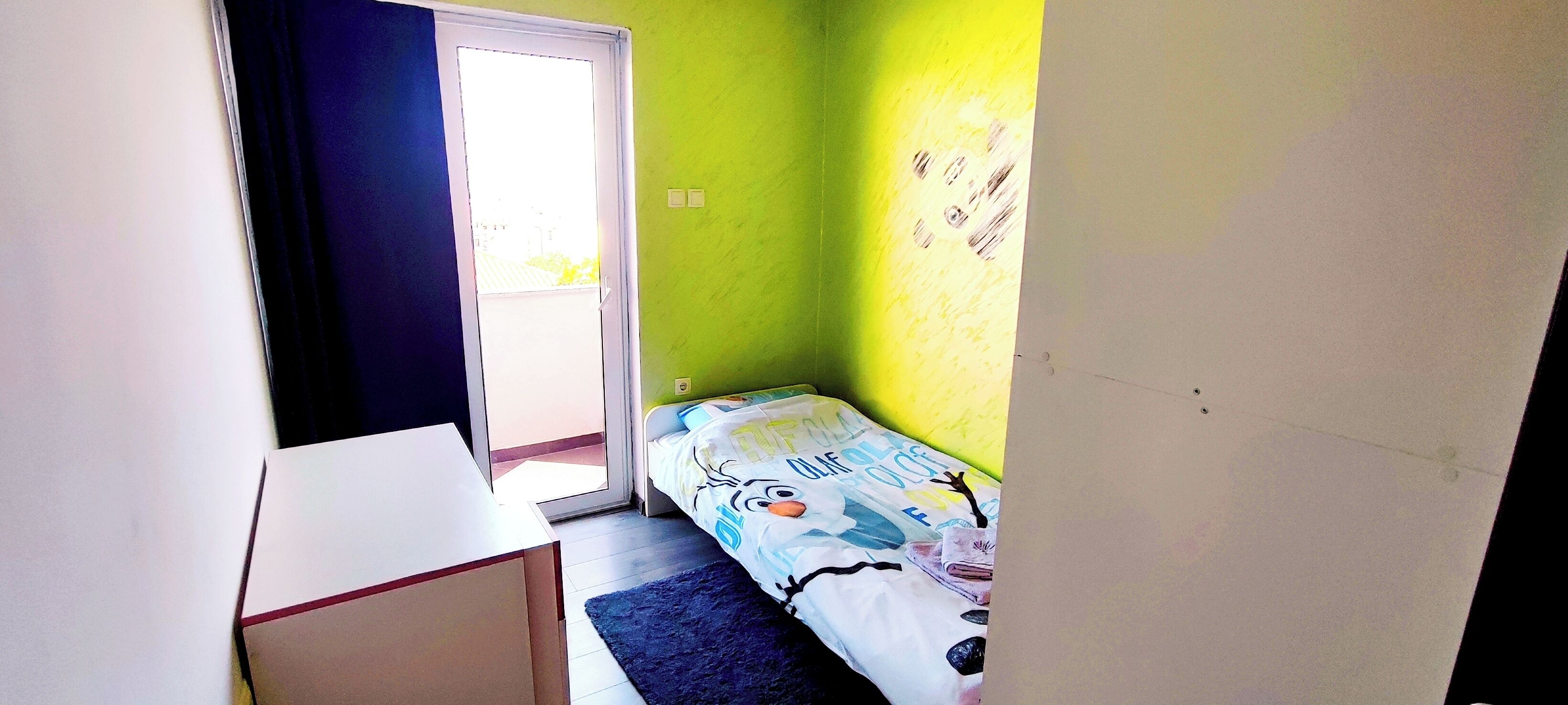 Una stanza piccola con un letto, una scrivania e una porta che dà sull'esterno.