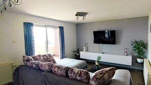 Ein modernes Hotelzimmer mit Schlafsofa, Flachbildfernseher, einem kleinen Tisch und einer Zimmerpflanze.