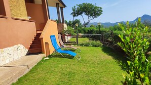 Une pelouse bien entretenue, agrémentée de deux fauteuils de jardin bleus, d’un mur en pierre et offrant une vue sur les montagnes en arrière-plan.