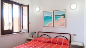 Une chambre à coucher comprenant un lit, une table de chevet, une lampe, une fenêtre avec des rideaux et deux tableaux encadrés accrochés au mur.